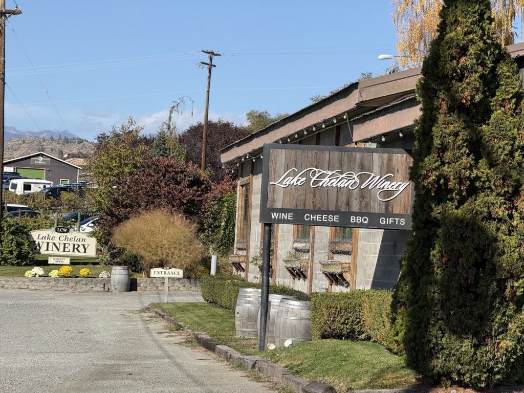 Lake Chelan Winery on Manson Highway, with its sign reading wine, cheese, BBQ and gifts, wine barrels and fall flowers at the entrance