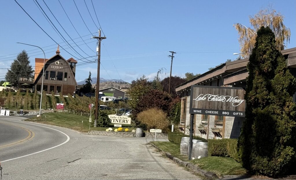 Lake Chelan Winery in the foreground, with its sign and tasting room beside the road, and the barn-style Cairdeas Winery building and vineyard in the background in the Lake Chelan Valley